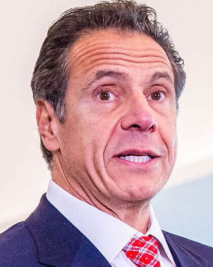 Photo of Andrew Cuomo, his face taught, likely in the middle of telling a bald-faced lie. He is wearing a blue jacket, white shirt, and red tie