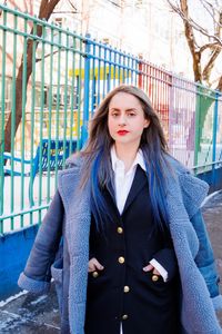 Photo of Corinne Fisher standing in front of a fence  looking serious with winter coat on.