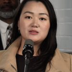 Photo of Julie Won looking into the camera, behind a microphone, with a camel-colored coat on, expressing concern for public transit users with disabilities