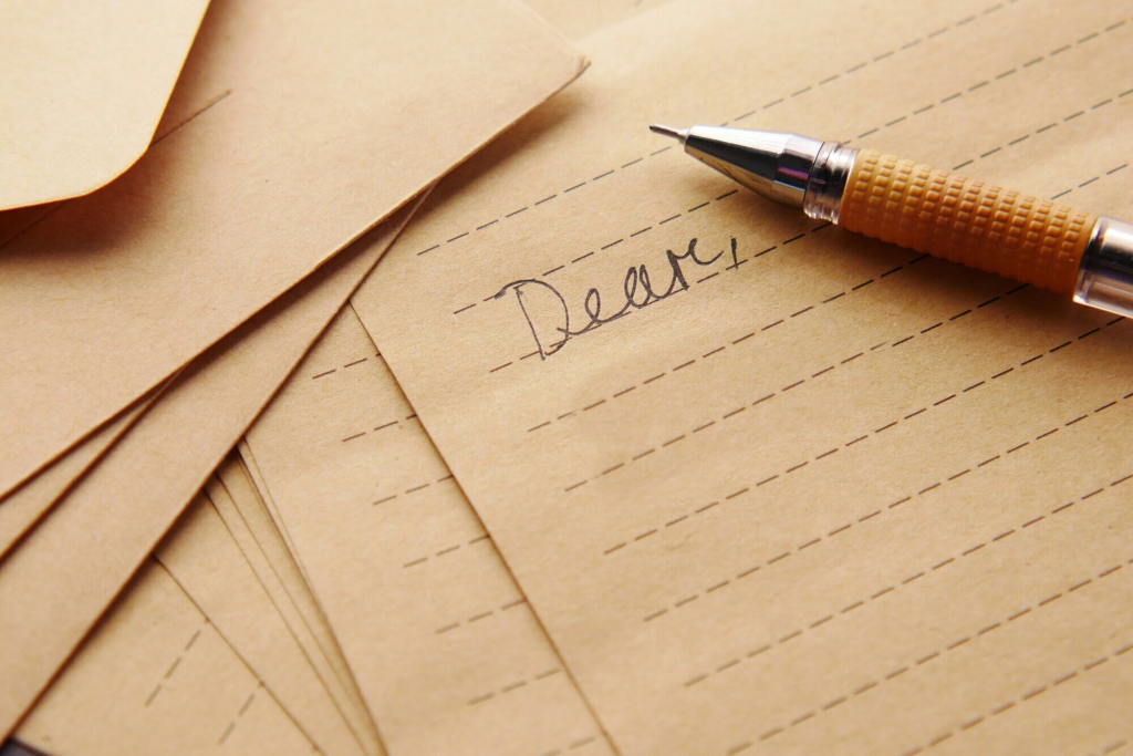 Photo of several pieces of lined paper with a mechanical pencil resting on top. One piece of paper has the beginning of a letter with just the word "Dear," written on it